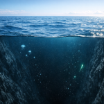 The ocean floor unexplored — a dark, bioluminescent deep-sea environment photographed from above, showing the vast unknown depths of Earth's oceans.